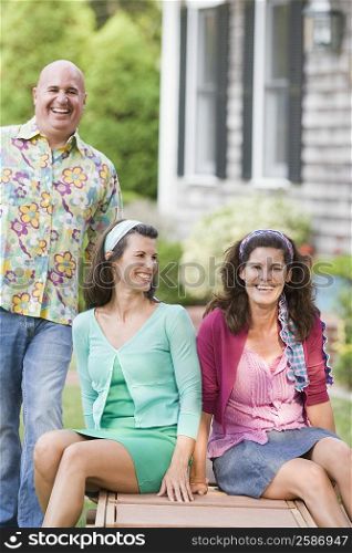 Two mature women sitting on a lounge chair with a mature man standing beside them