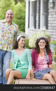 Two mature women sitting on a lounge chair with a mature man standing beside them