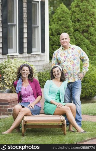 Two mature women sitting on a lounge chair with a mature man standing beside them