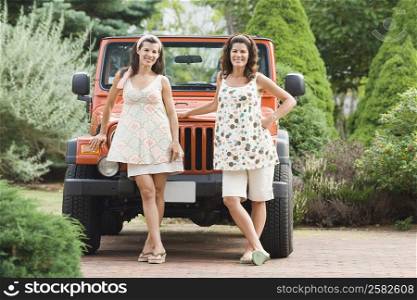 Two mature women standing in front of a jeep in a garden and smiling