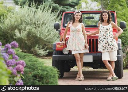 Two mature women standing in front of a jeep in a garden and smiling