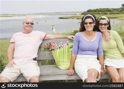 Two mature women with a mature man sitting on a bench and smiling