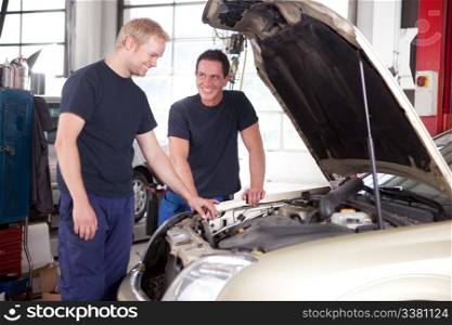 Two mechanics looking at and working on a car in a repair shop