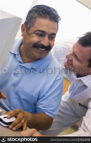 Two men at computer smiling and looking at each other (high key)