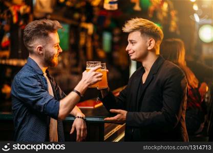 Two men at the bar counter raised their glasses with beer for the victory in game in a sport pub, happy leisure of football fans
