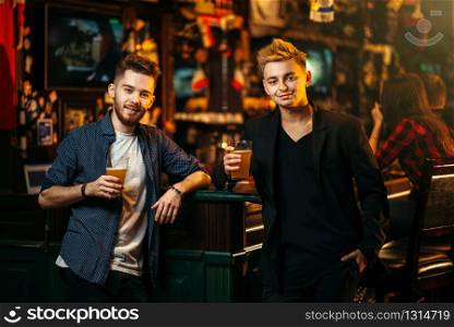Two men at the bar counter raised their glasses with beer for the victory in game in a sport pub, happy leisure of football fans. Men raised their glasses with beer in a sport pub