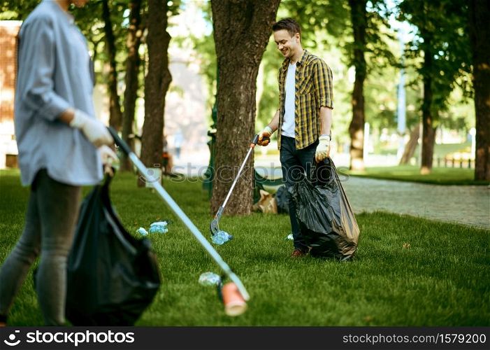 Two men collects plastic garbage in bags in park, volunteering. Male person cleans forest, ecological restoration, eco lifestyle, trash collection and recycling, ecology care, environment cleaning. Two men collects plastic garbage, volunteering