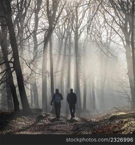two men hike in early morning misty winter forest with sun beams near utrecht in the netherlands