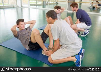 Two men holding feet of friends doing situps