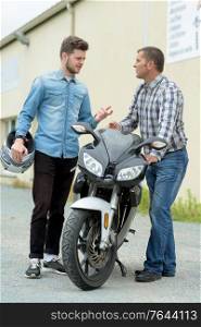 two men in conversation stood beside a motorbike
