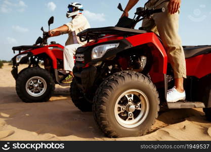 Two men in helmets and glasses ride on atv in desert. Male persons on quad bikes, sandy race, dune safari in hot sunny day, 4x4 extreme adventure, quad-biking. Men in helmets and glasses ride on atv in desert