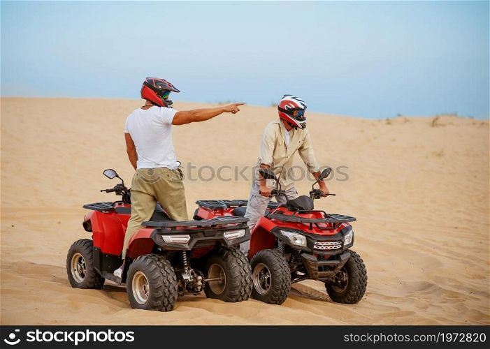 Two men in helmets, freedom atv riding in desert sands. Male persons on quad bikes, sandy race, dune safari in hot sunny day, 4x4 extreme adventure, quad-biking. Two men in helmets, atv riding in desert sands