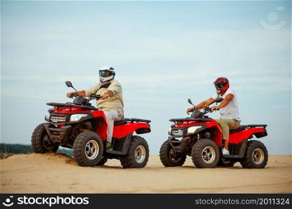Two men in helmets, freedom atv riding in desert sands. Male persons on quad bikes, sandy race, dune safari in hot sunny day, 4x4 extreme adventure, quad-biking concept. Two men in helmets, atv riding in desert sands