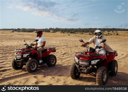 Two men in helmets ride on atv in desert. Male persons on quad bikes, sandy race, dune safari in hot sunny day, 4x4 extreme adventure, quad-biking. Two men in helmets ride on atv in desert