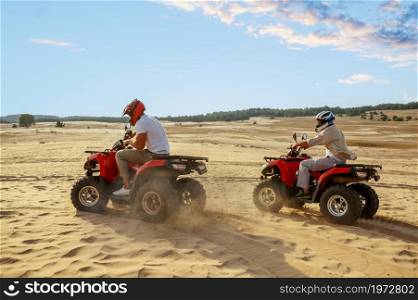 Two men in helmets ride on atv in desert. Male persons on quad bikes, sandy race, dune safari in hot sunny day, 4x4 extreme adventure, quad-biking. Two men in helmets ride on atv in desert