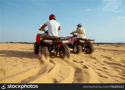 Two men in helmets riding on atv in desert sands, back view. Male persons on quad bikes, sandy race, dune safari in hot sunny day, 4x4 extreme adventure, quad-biking. Two men in helmets riding on atv in desert sands