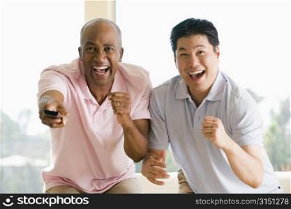 Two men in living room with remote control cheering and smiling