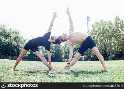 Two men poised in leaning sideways yoga position in park