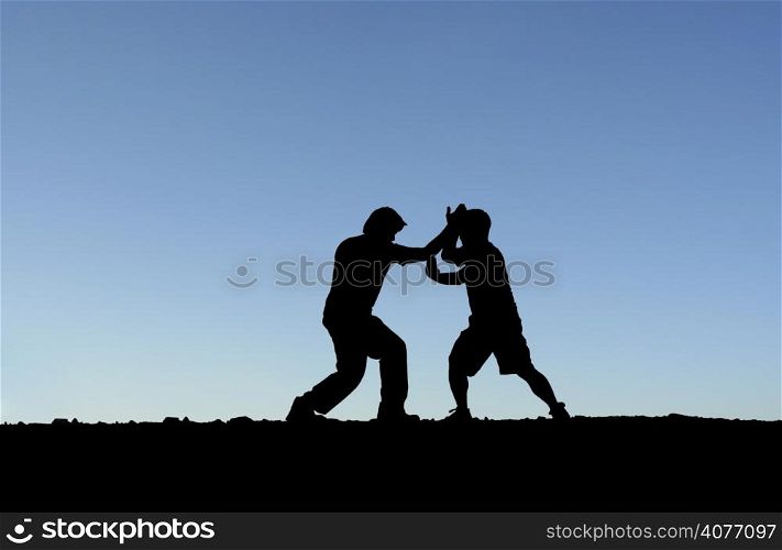 Two men practicing martial arts on top of a mountain (in silhouette)
