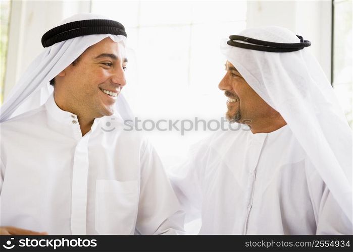 Two men sitting indoors talking and smiling (high key)
