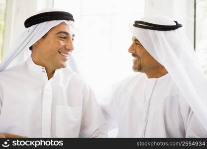 Two men sitting indoors talking and smiling (high key)