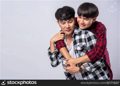 Two men who love each other hug from behind another.