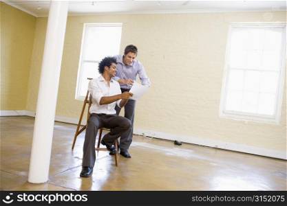Two men with ladder in empty space looking at paper