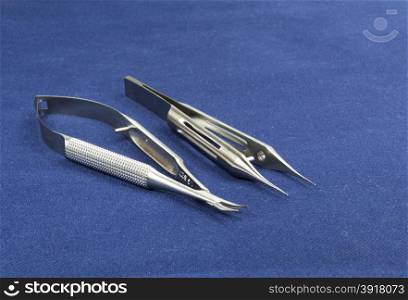Two microsurgical instruments on blue background , sidelong view.Scissors,soft curve and forceps with platform