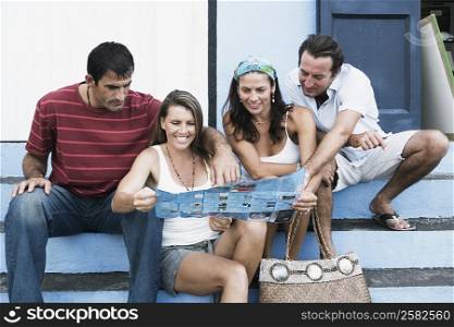 Two mid adult couples sitting on steps and looking at a brochure