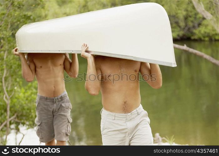 Two mid adult men carrying a canoe on their heads