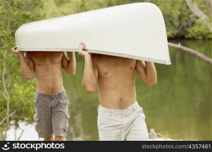 Two mid adult men carrying a canoe on their heads