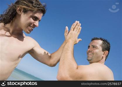 Two mid adult men giving high-five to each other