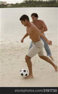Two mid adult men playing soccer on the beach