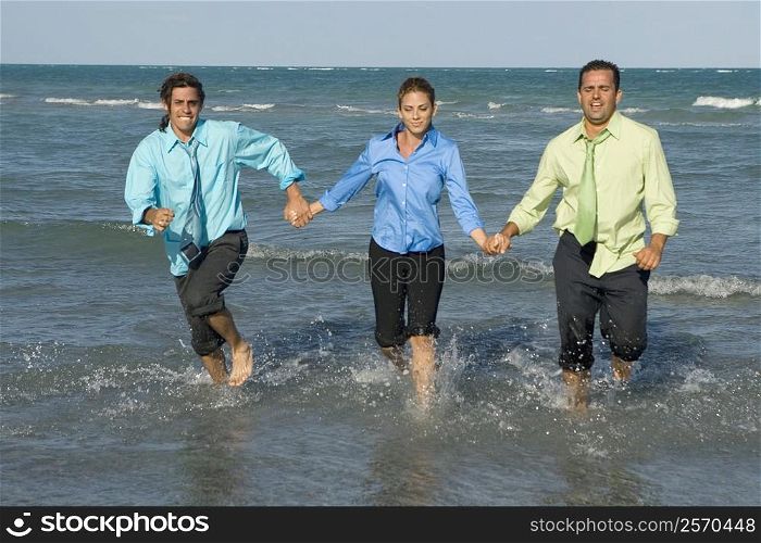 Two mid adult men running with a mid adult woman on the beach