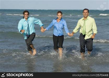 Two mid adult men running with a mid adult woman on the beach