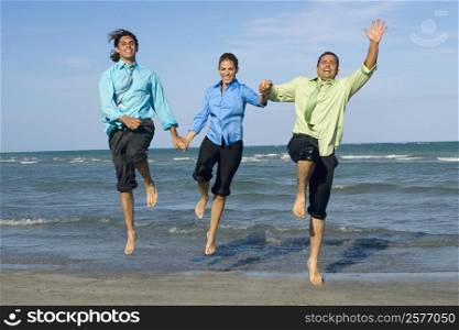 Two mid adult men with a mid adult woman holding each other&acute;s hands and jumping on the beach