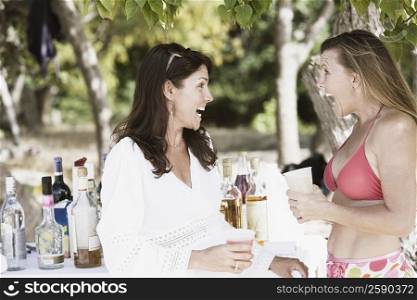 Two mid adult women drinking wine on the beach