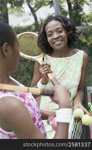 Two mid adult women holding tennis rackets and smiling in a court
