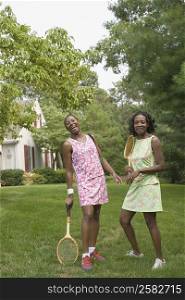 Two mid adult women holding tennis rackets and smiling in a lawn