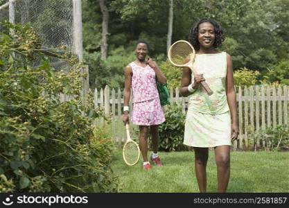 Two mid adult women holding tennis rackets and walking in a lawn