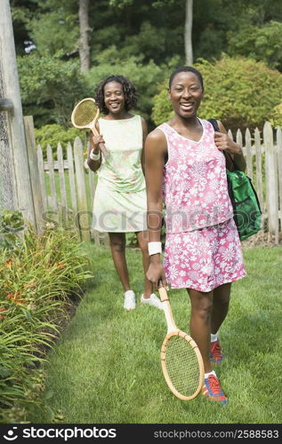 Two mid adult women holding tennis rackets and walking in a lawn