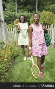 Two mid adult women holding tennis rackets and walking in a lawn