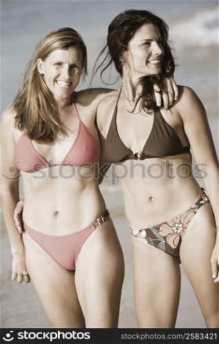 Two mid adult women standing with their arms around each other on the beach