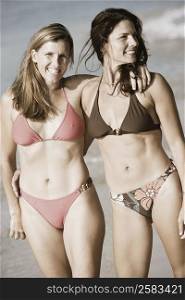 Two mid adult women standing with their arms around each other on the beach