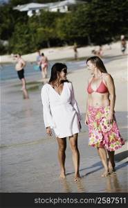 Two mid adult women walking on the beach with tourists in the background