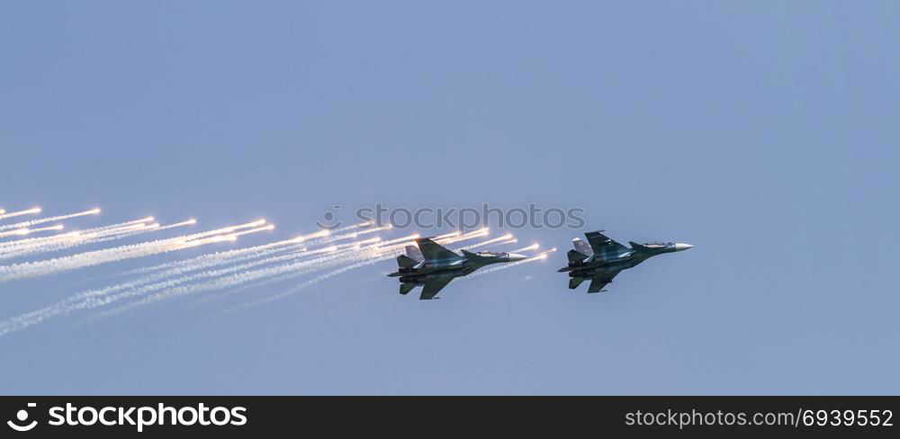 Two military aircrafts flying in the blue sky. Aircraft fighter flies and shoots heat guns in the blue sky...