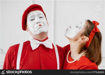 Two mime artists in red costumes, kissing scene. Pantomime theater, parody comedian, positive emotion, humour performance, funny face mimic and grimace. Two mime artists in red costumes, kissing scene