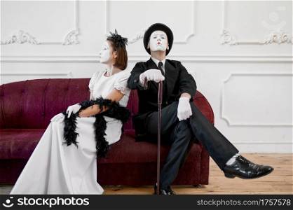 Two mime artists, lady and gentleman sitting on sofa. Pantomime theater, parody comedian, positive emotion, humour performance, funny face mimic and grimace. Mime artists, lady and gentleman sitting on sofa