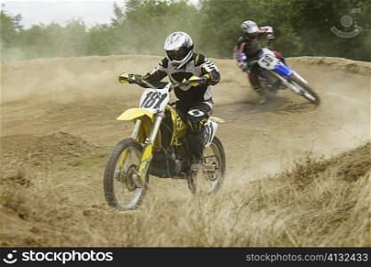 Two motocross riders riding motorcycles on a dirt road