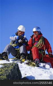 Two mountain climbers sitting on snowy mountain drinking from thermos and smiling (selective focus)